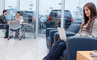 A girl sitting inside a dealership, looking at her computer.